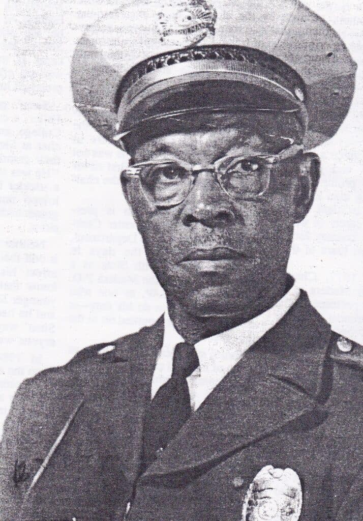 African American military officer in uniform, wearing glasses and a cap.