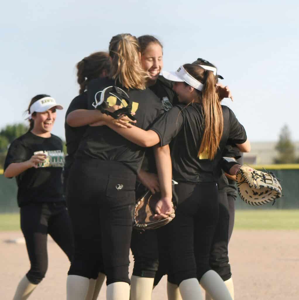 Girls' softball team celebrating victory on the field after a game.