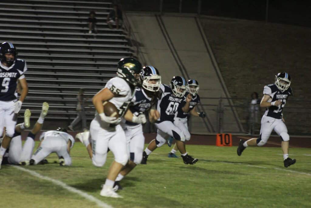 Madera high school football players running on the field during a game.