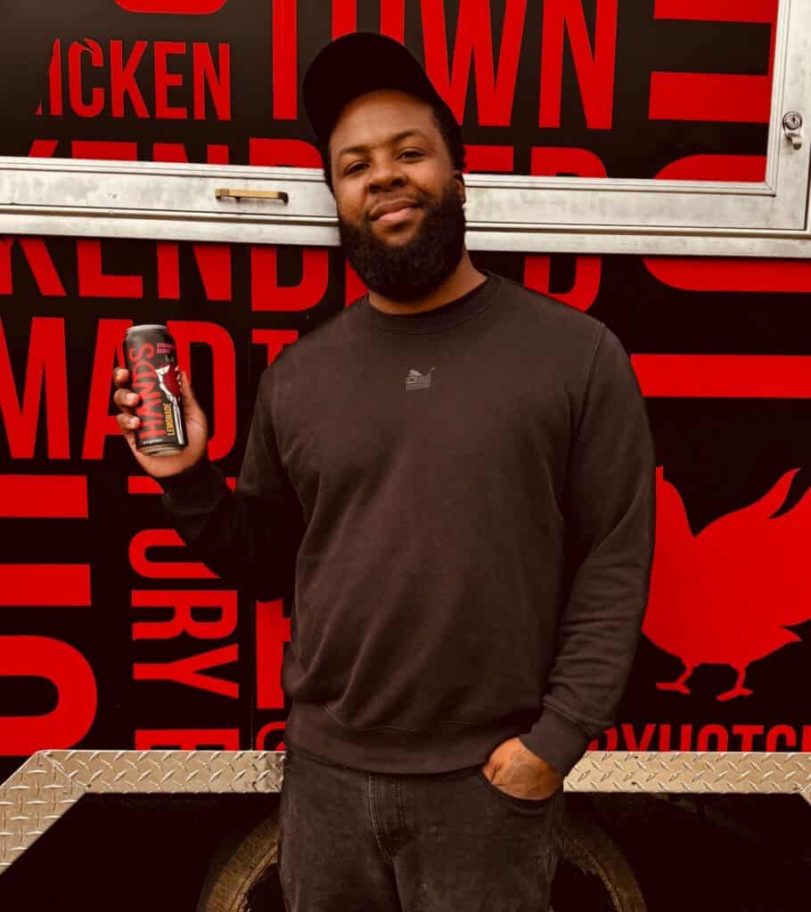 Man holding a can of soda in front of Chicken Town food truck.