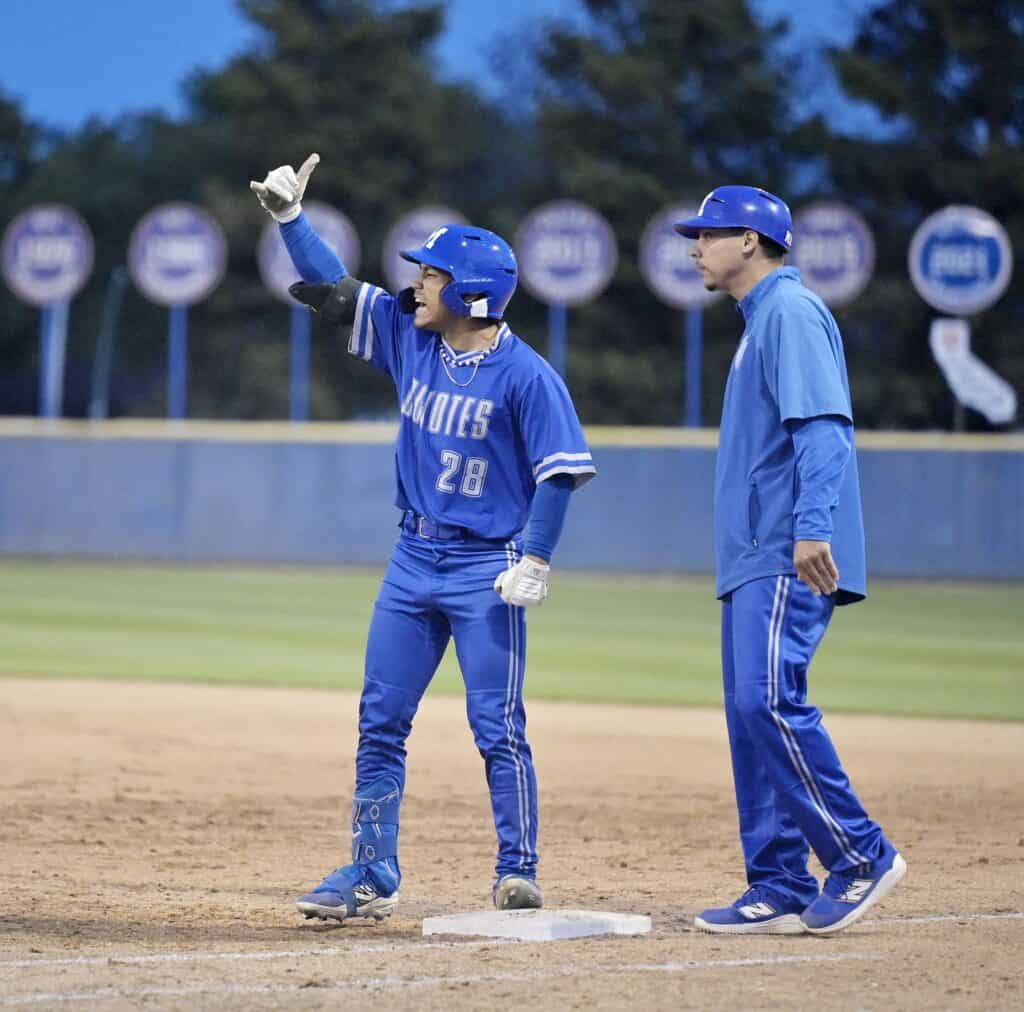 Baseball player in blue uniform celebrating with coach during game.