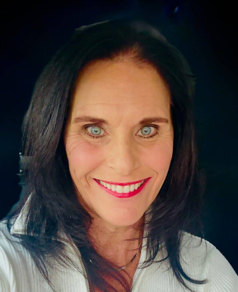 Woman with dark hair and blue eyes smiling, wearing a white top.