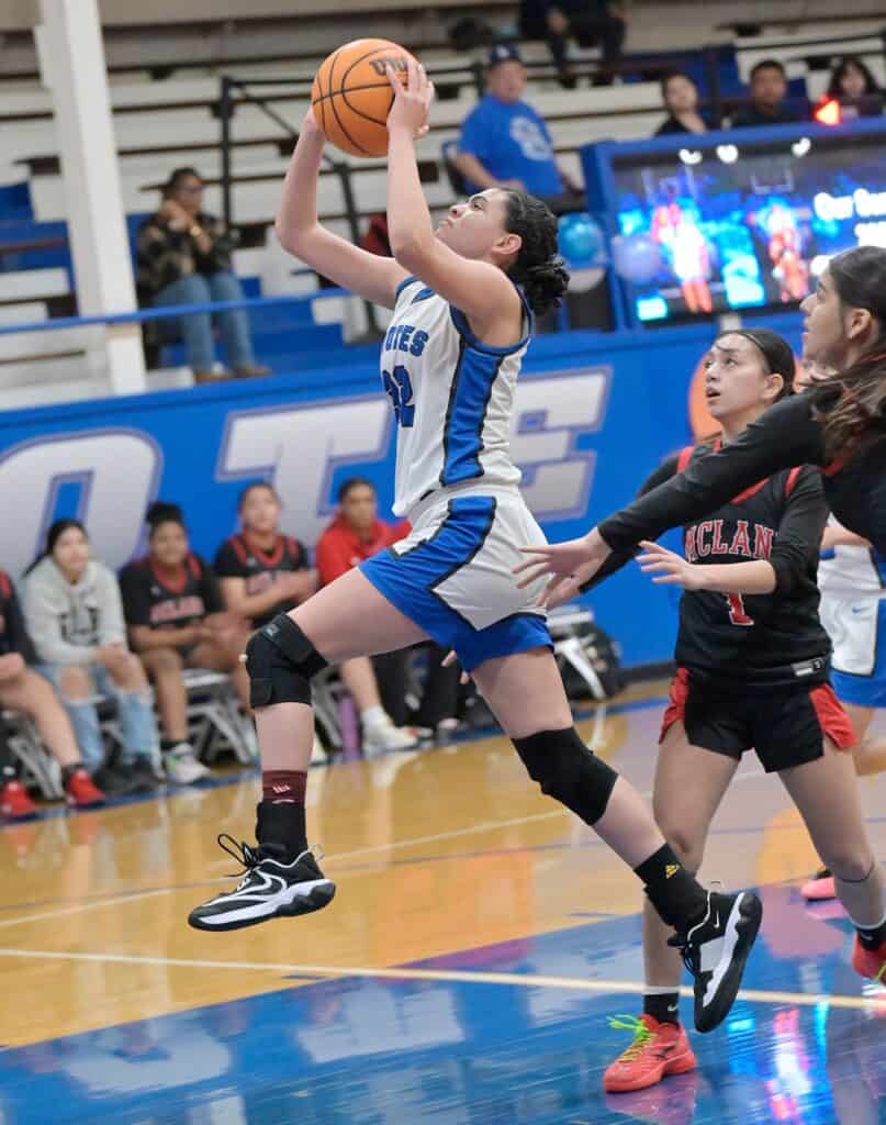 Young female basketball player jumping for shot during game.