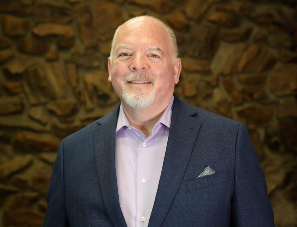 Madera Tribune business leader smiling in a suit against a stone wall.