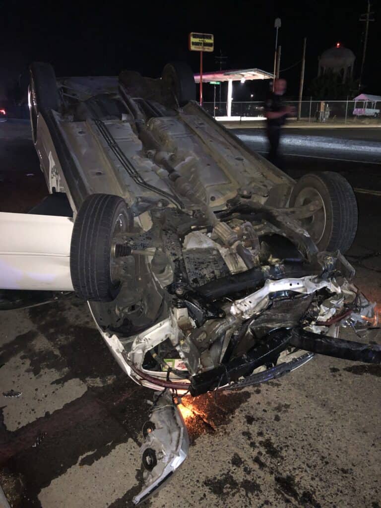 Overturned car crash on dark street, showing severe damage and debris from the accident.