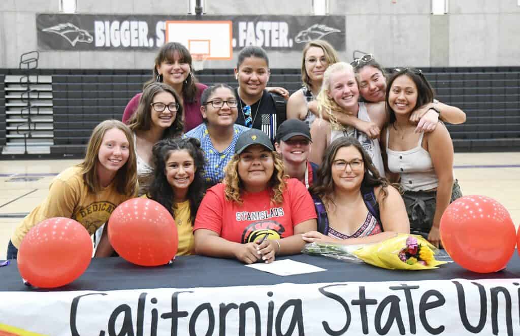 Diverse group of students gathered around a table with balloons and flowers, celebrating at a school.