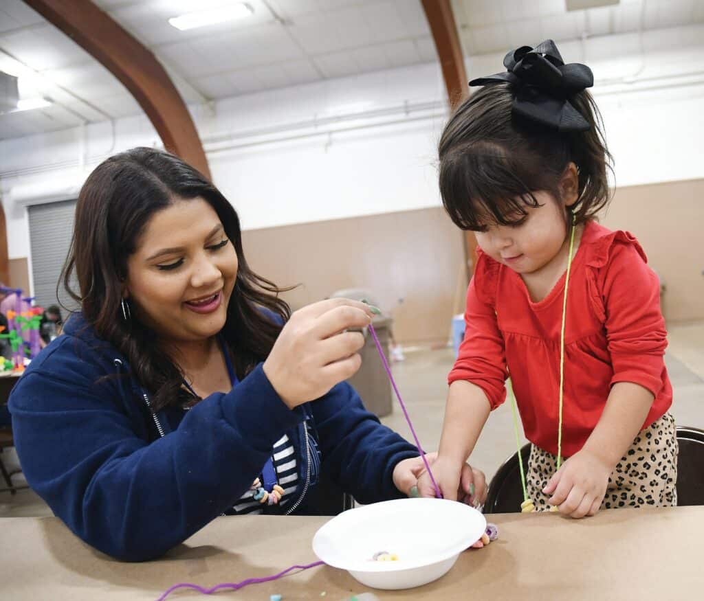 Young girl and woman engaging in a craft activity with yarn.