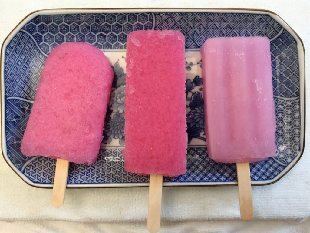 Colorful homemade fruit popsicles on a patterned plate, ideal for hot weather enjoyment.