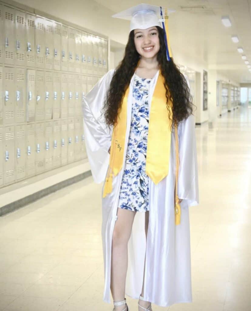 Graduating student in cap and gown at Madera High School hallway.