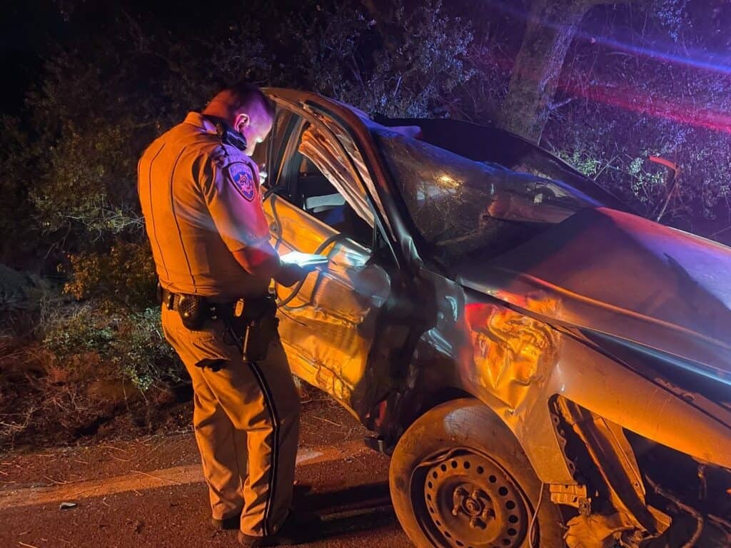 Emergency responder examines a damaged car after a nighttime crash.
