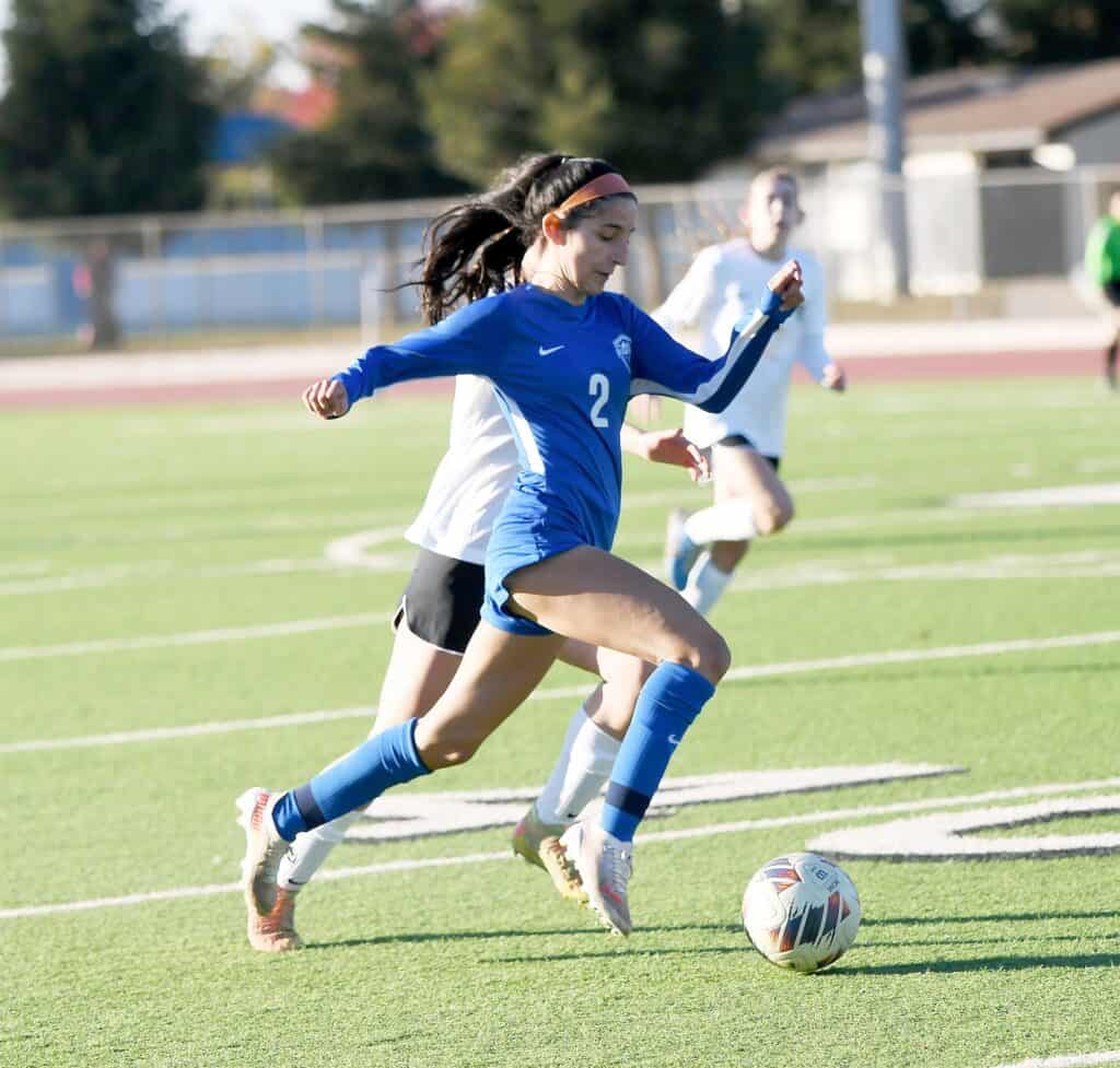 Female soccer player running with ball on field.