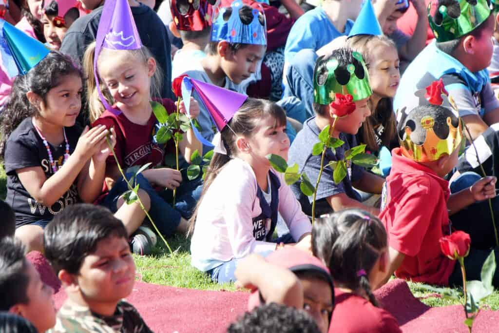 Children celebrating at a party with colorful hats and flowers outdoors.