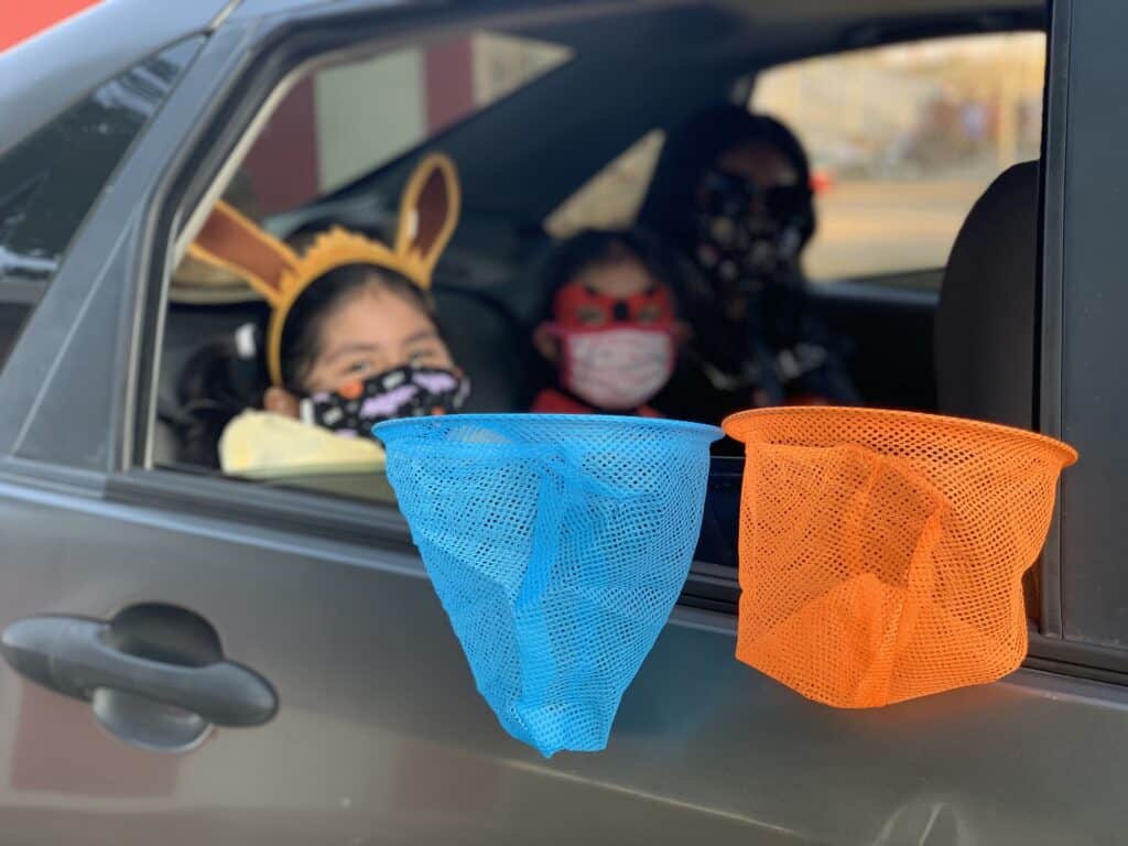Children with Halloween costumes in car, holding colorful treat bags.