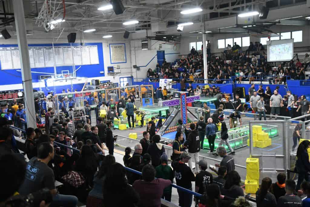 Robotics competition with students and teams competing in a large indoor gymnasium.