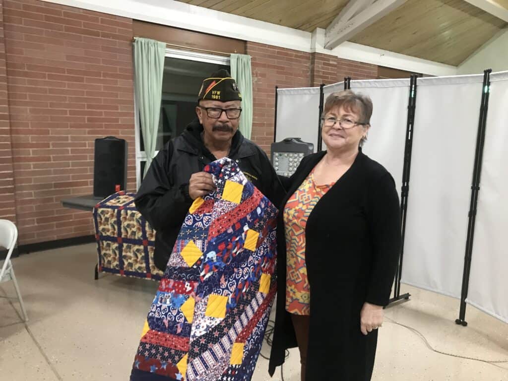 Veteran and woman holding a colorful quilt at Madera Veterans Day event.