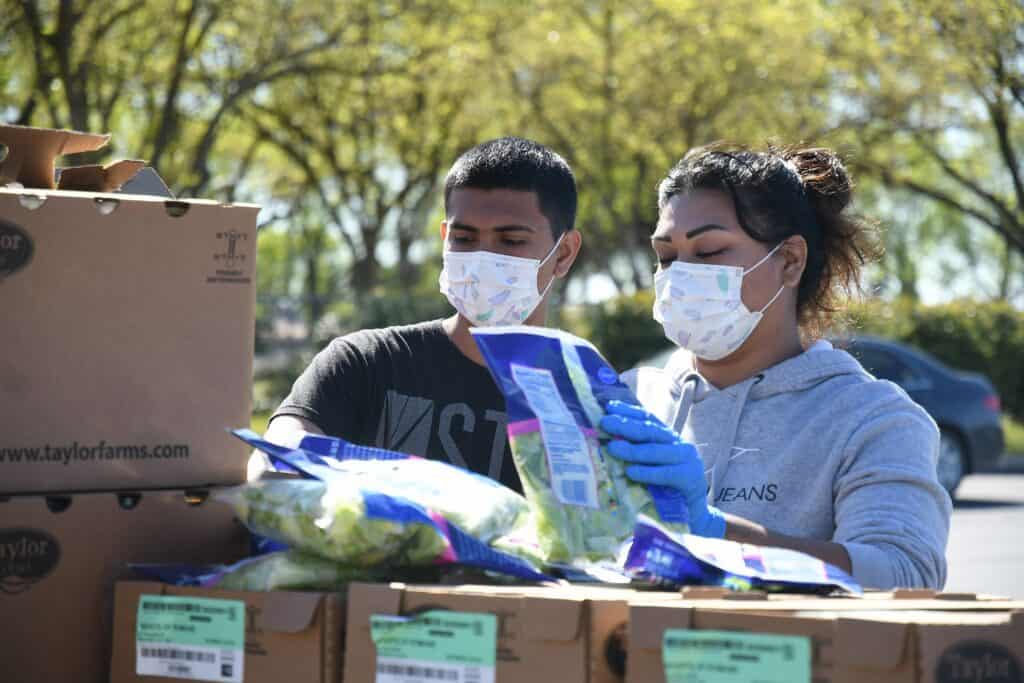 Volunteers wearing masks and gloves distribute food packages outdoors in Madera.
