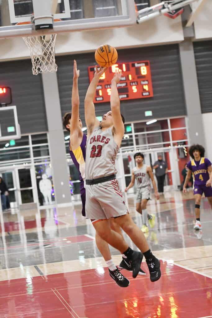 Female basketball player in white jersey jumping for shot in indoor game.