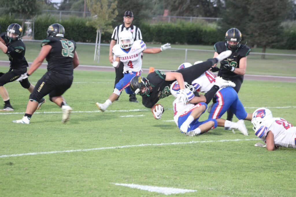 Youth football players tackling during a game on a grassy field.