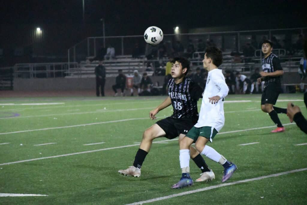 Youth soccer players competing on the field at night under stadium lights.