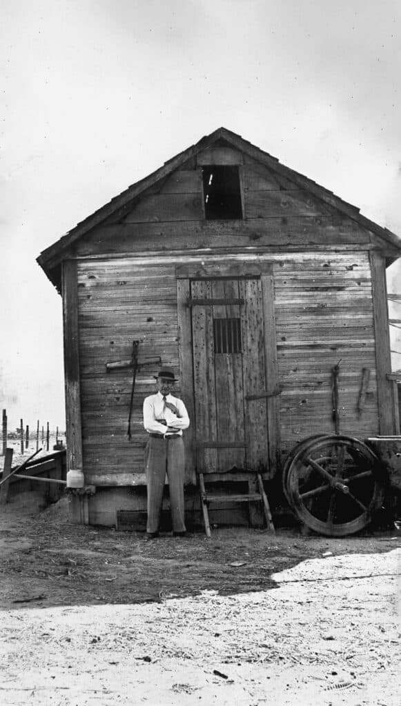 Old wooden barn with a man standing outside, showcasing early rural architecture.