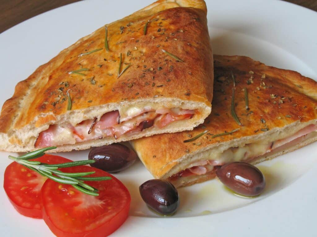Calzone with ham, cheese, and herbs, served with tomato and olives.