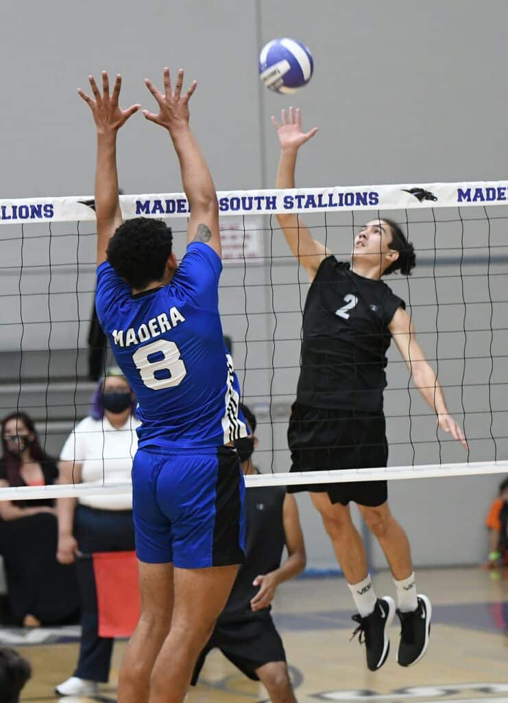 Madera volleyball player spikes ball against opponent at the net.
