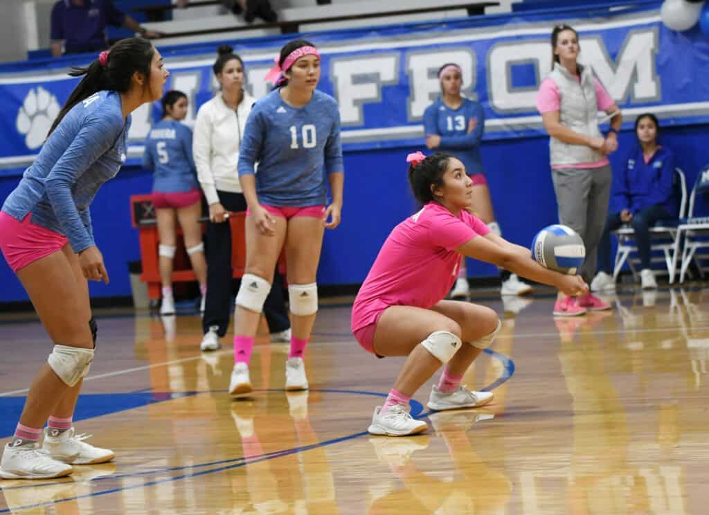 Volleyball player in pink prepares to serve during a match at Madera High School gym.