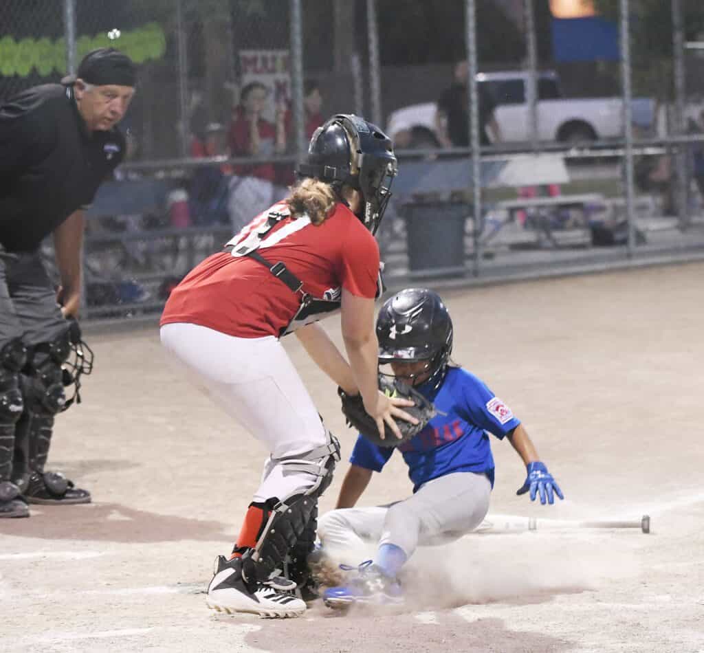 Jugador de béisbol deslizándose hacia home con el cátcher y el árbitro cerca durante un partido.