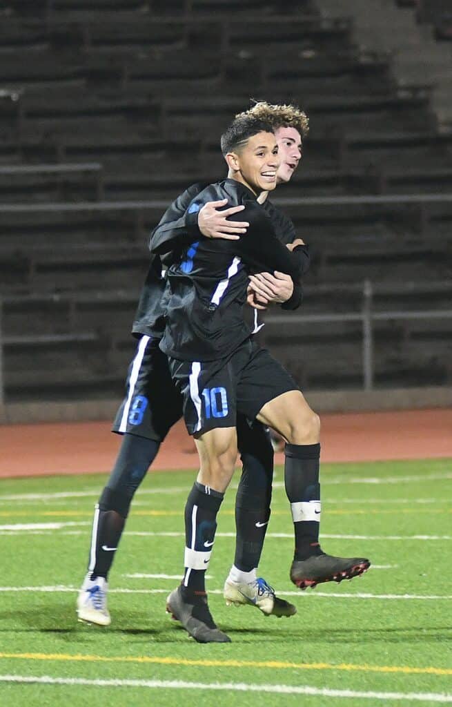 Two young soccer players celebrating on the field after scoring.