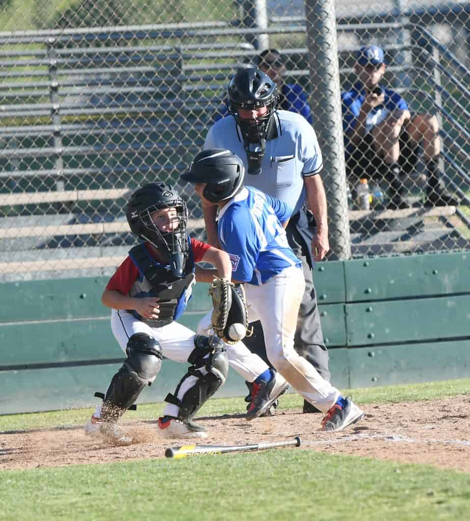 Young baseball player sliding into home plate with catcher and umpire nearby.