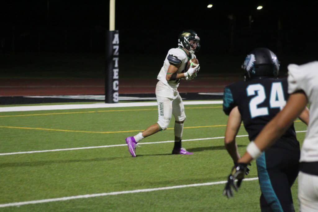 Madera High School football player running with the ball during a night game.