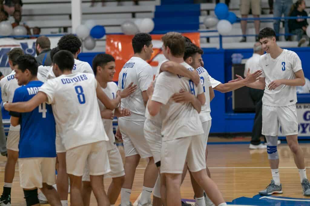 High school volleyball team celebrating victory on the court.