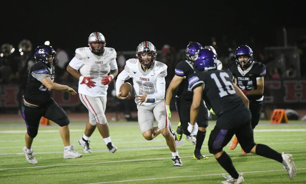 Madera High football player running with ball during a night game.