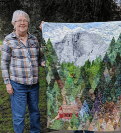 Woman holding a colorful mountain landscape quilt outdoors.