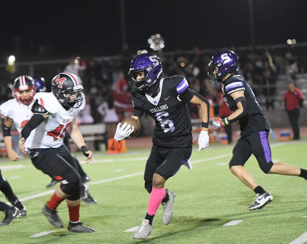 Youth football game with players in action on the field at night.