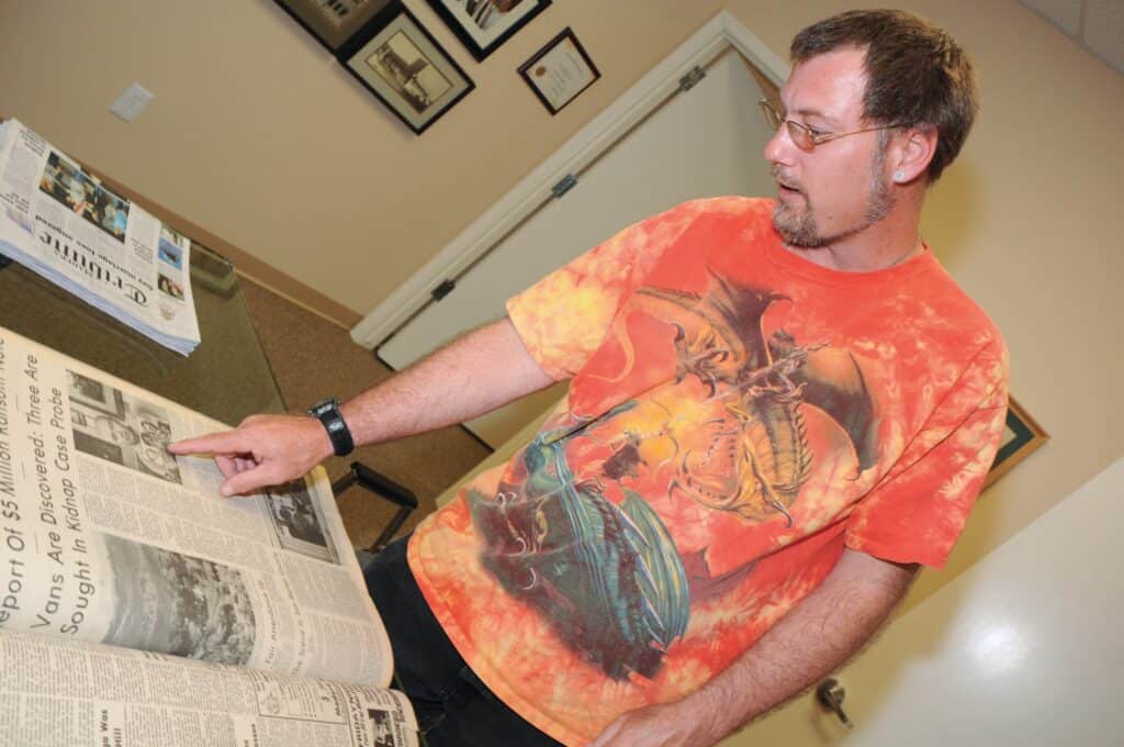 Man reading and pointing at newspaper in an office setting.