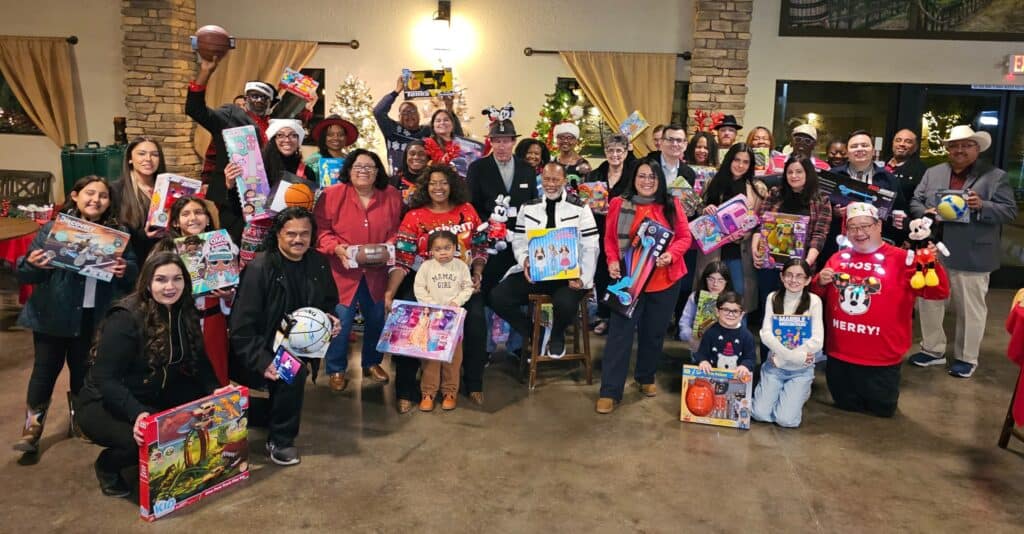 People gathered indoors holding holiday gifts and smiling.