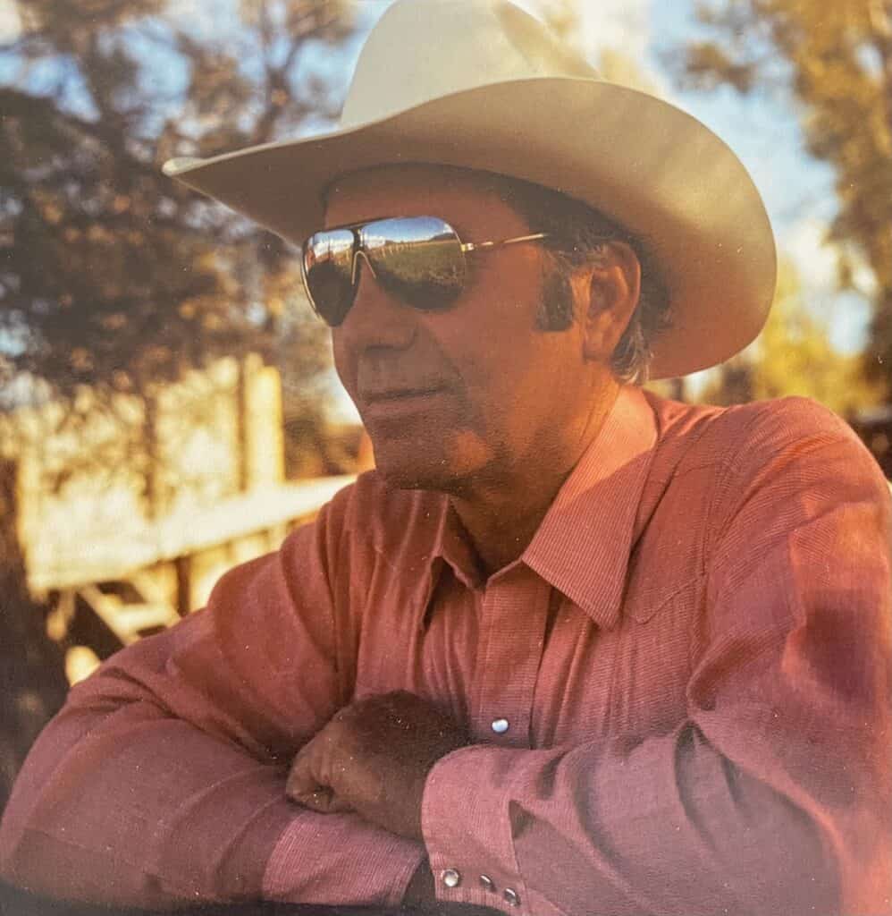 Man in cowboy hat and sunglasses outdoors in warm sunlight.