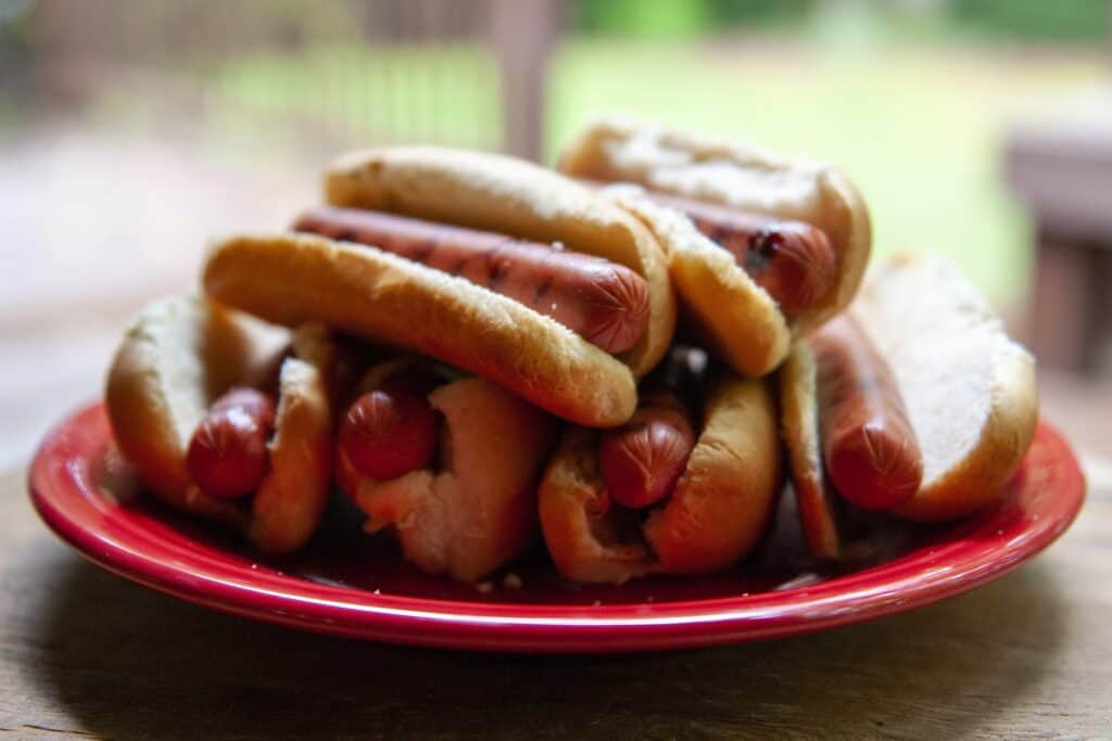 Hot dog sandwiches with buns, hot dogs, and toppings on a red plate.