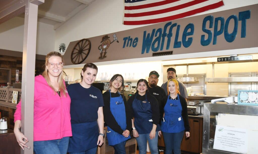 Waffle Spot staff smiling in front of the restaurant sign at The Madera Tribune.