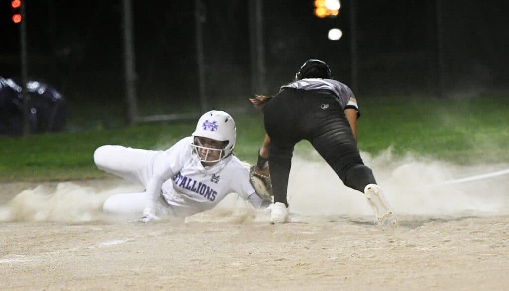 Baseball player sliding into a base while another player tries to tag him out.