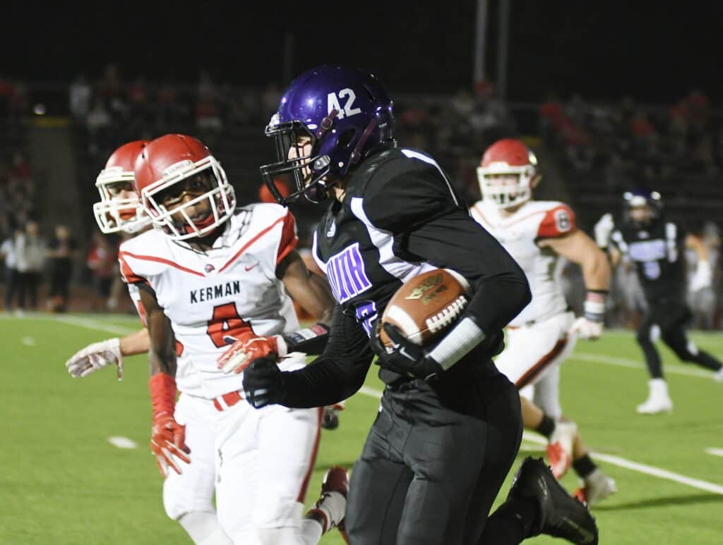 High school football game with players in action on the field.