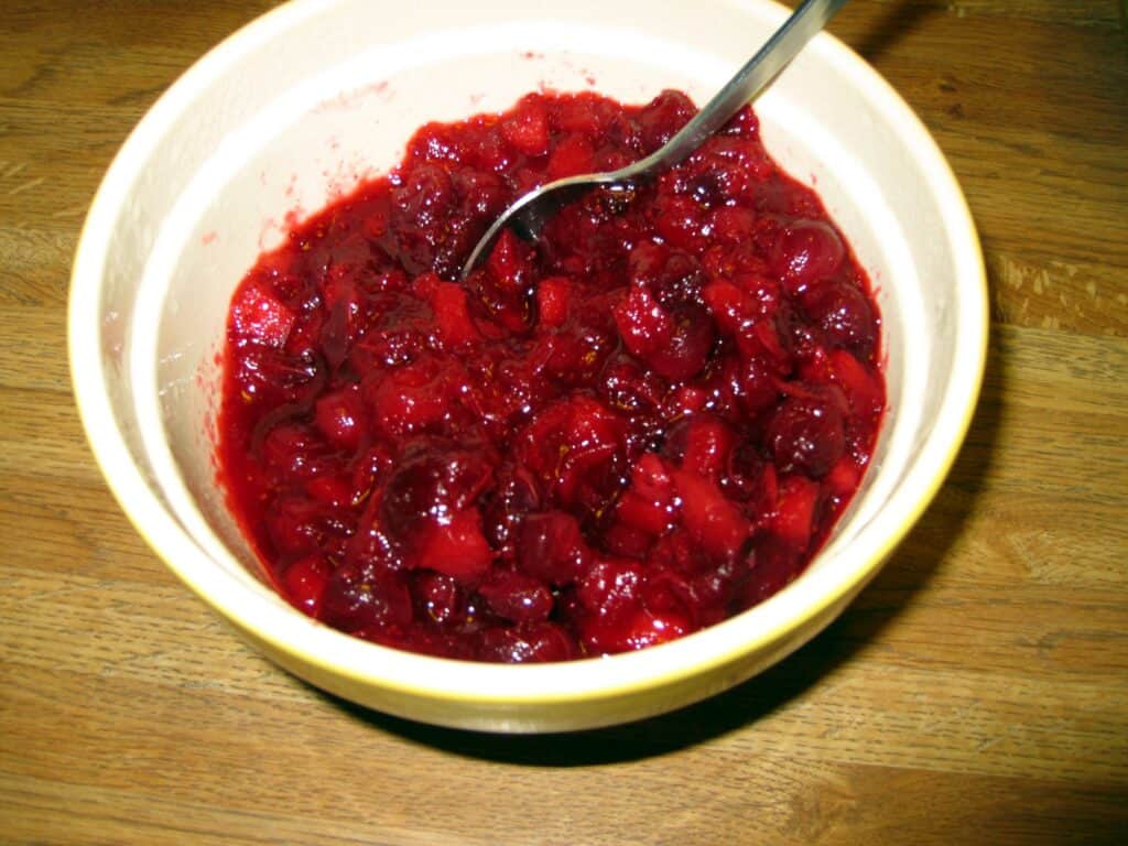 Cherry jam in a white bowl with a spoon, on a wooden table.