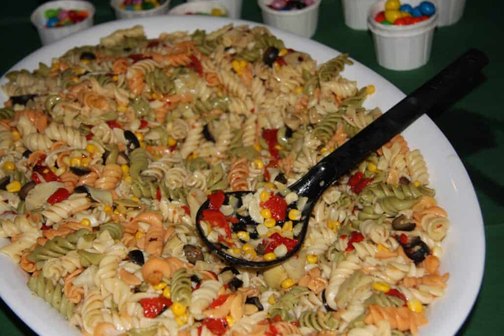 Pasta salad with colorful vegetables and black olives on a white platter.