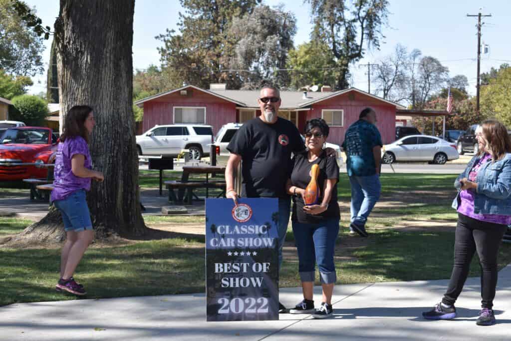People at the Madera Classic Car Show holding a "Best of Show" sign in a park.