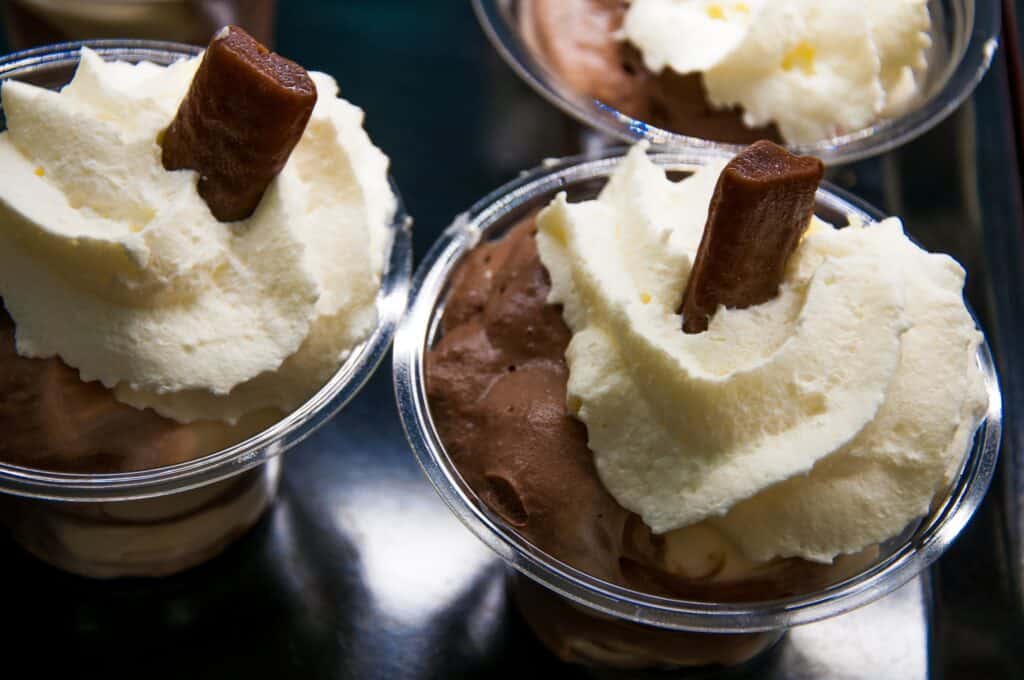Ice cream cups with chocolate and vanilla flavors topped with whipped cream and chocolate sticks.