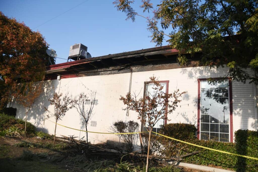 Madera Tribune building with damaged roof and exterior, surrounded by trees and autumn foliage.