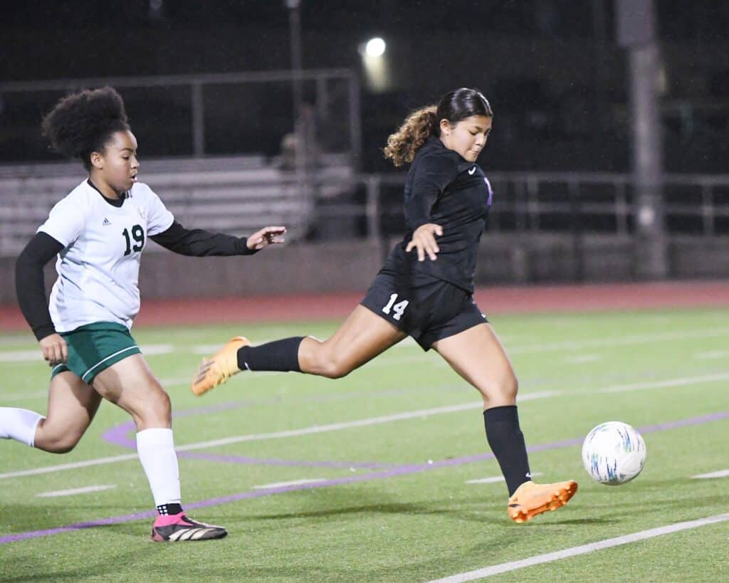 Girls soccer player kicking ball during night game.