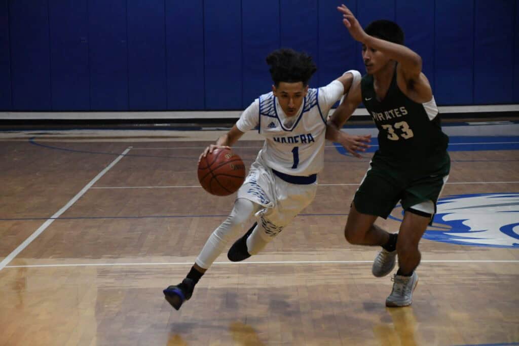 Young basketball player dribbling past defender on court.