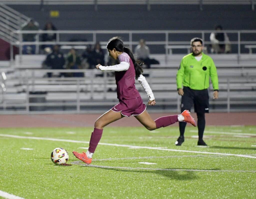 Female soccer player kicking ball on field.